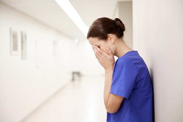sad or crying female nurse at hospital corridor