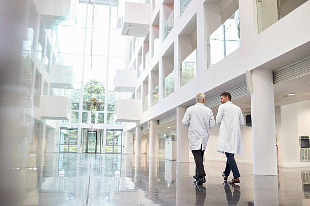 Rear View Of Doctors Talking As They Walk Through Hospital